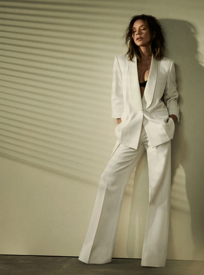 a woman in a white suit leans against a wall