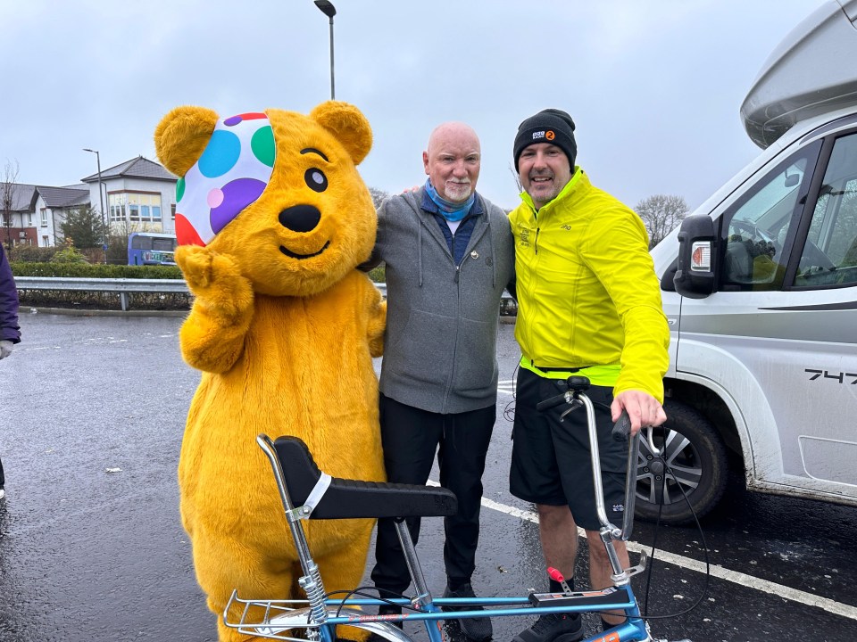 a man in a yellow jacket stands next to a teddy bear