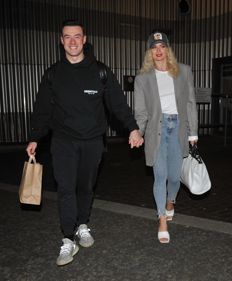 a man wearing a black essentials hoodie holds hands with a woman