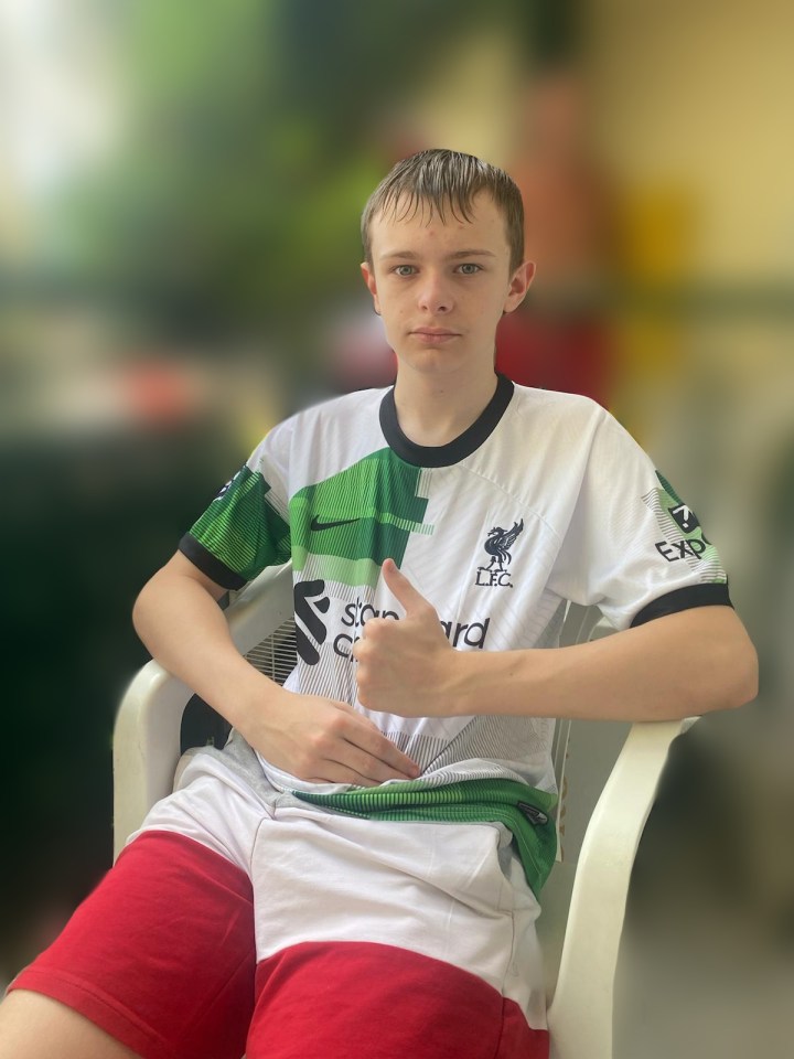 a boy wearing a white and green liverpool shirt gives a thumbs up
