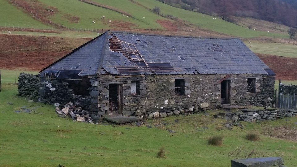 a stone building with a slate roof is in the middle of a grassy field
