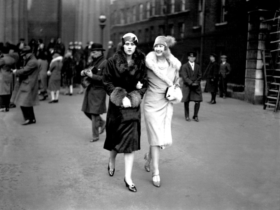 a black and white photo of two women walking down a street