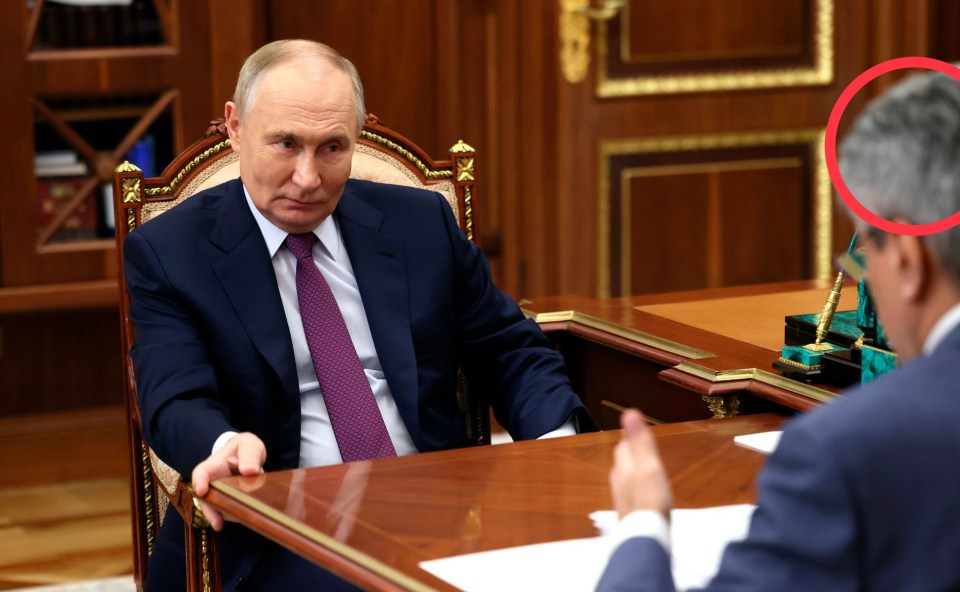 a man in a suit and tie sits at a desk talking to another man