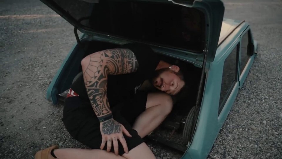 a man with a tattoo on his arm is laying in the trunk of a car
