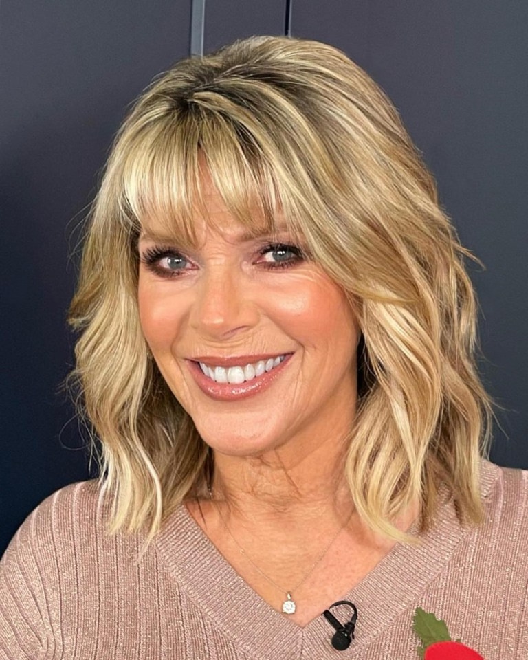 a woman wearing a sweater and a necklace smiles for the camera
