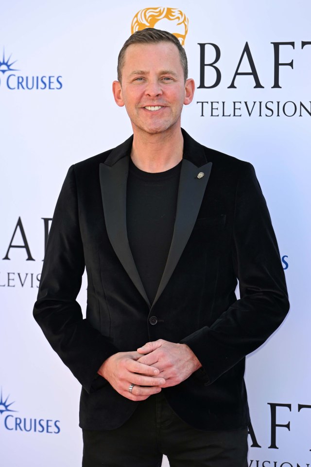 a man in a black suit stands in front of a bafta television sign