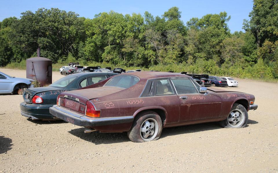 A maroon Jaguar XJS in a junkyard.