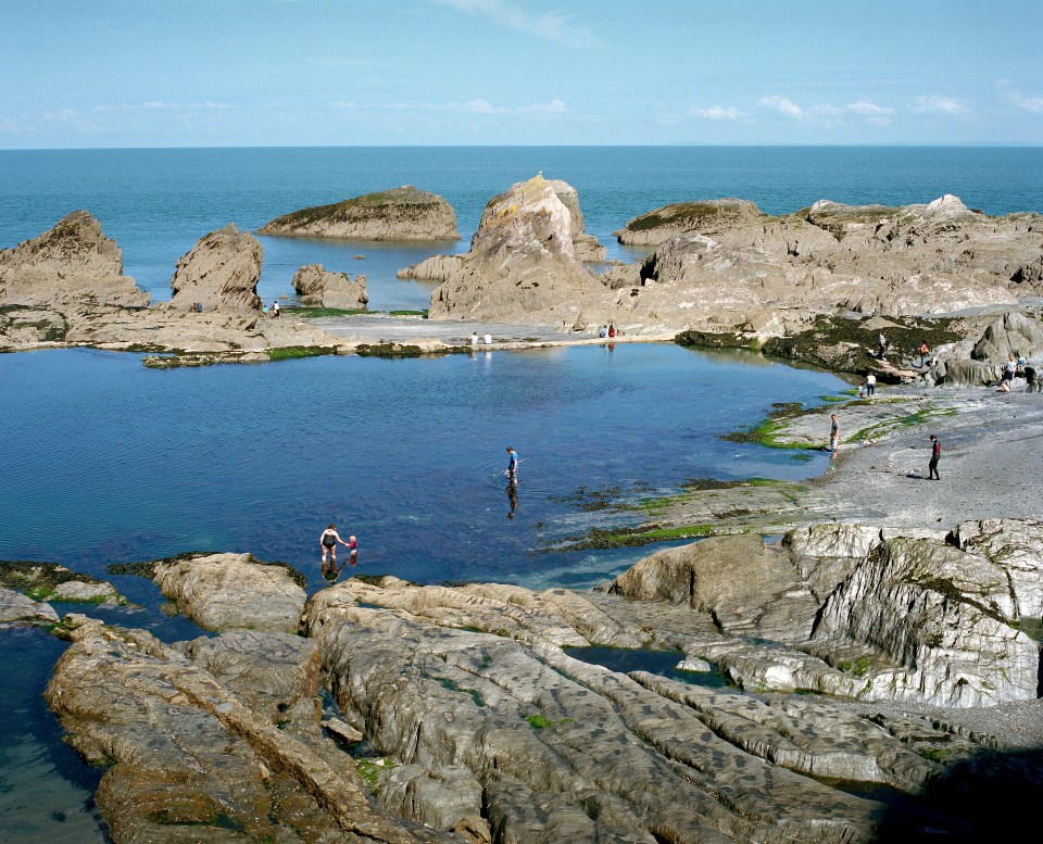 People swimming in a natural tidal pool on a rocky coast.
