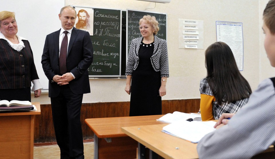 Vladimir Putin visiting a Russian high school classroom with a Leo Tolstoy portrait in the background.
