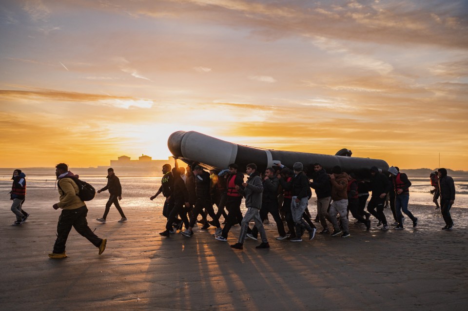 Migrants carry a smuggling boat on a beach at sunset.