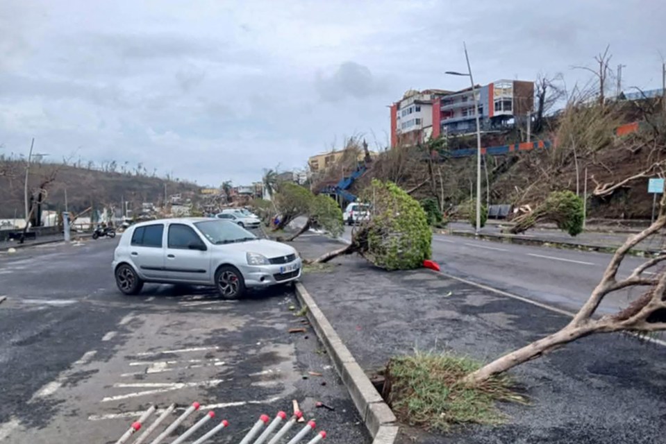 Cyclone damage in Mamoudzou, Mayotte, showing uprooted trees and a car.