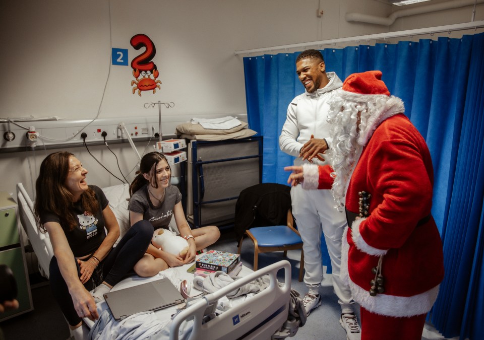 Anthony Joshua, Santa Claus, and a young patient and her mother at a children's hospital ward.