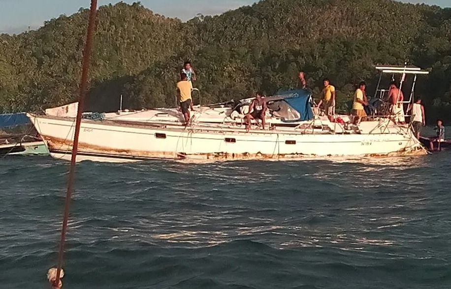 A damaged white yacht with several people on board, floating in the ocean.