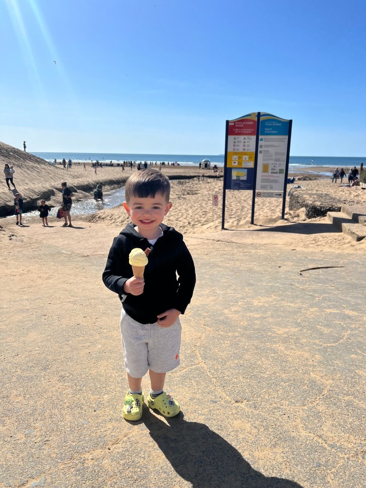 Toddler holding ice cream cone on beach.