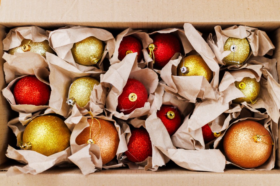 Box of red and gold Christmas ornaments wrapped in brown paper.