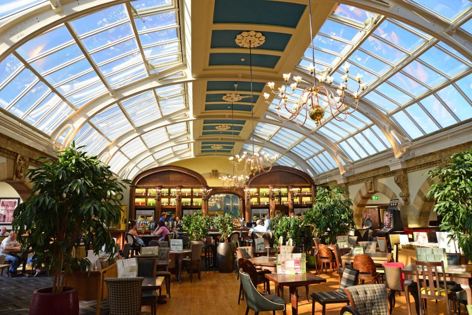 Interior of a pub with a glass ceiling and chandeliers.