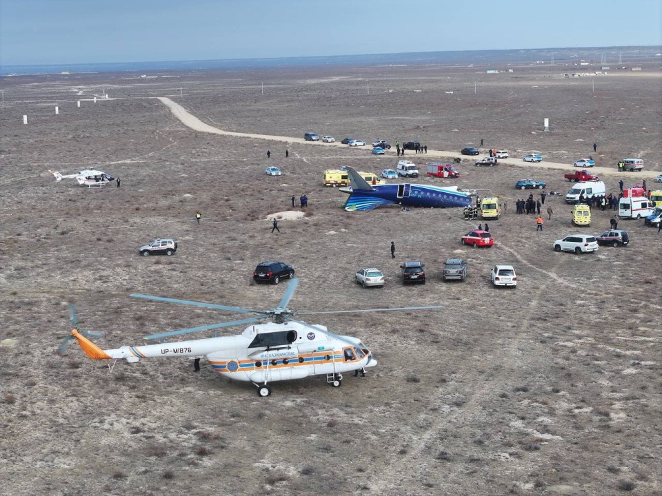 Drone view of an airplane crash site with emergency personnel and vehicles.