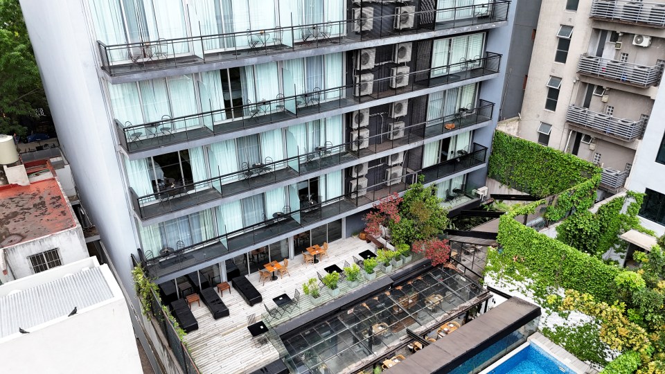 Drone view of a hotel with multiple floors, balconies, and a rooftop terrace.