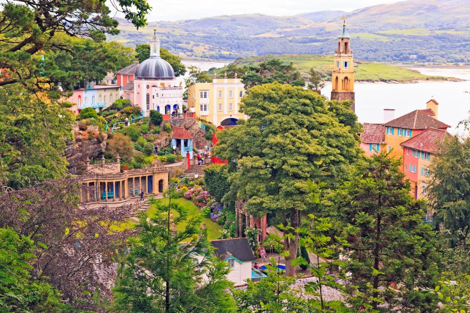 View of Portmeirion village in Wales, showing colorful buildings, a coast, and a tower.