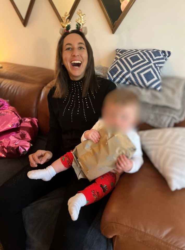 A woman wearing reindeer antlers holds a baby who is holding a gift.