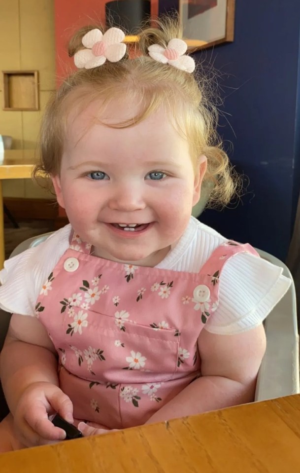 Smiling baby girl wearing a pink floral jumpsuit.
