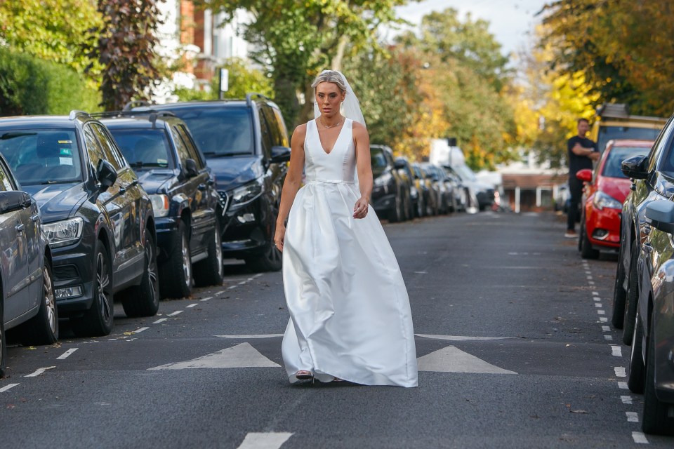 A bride in a white wedding dress walks down a residential street.