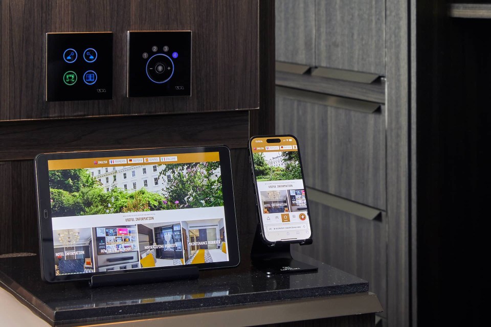 Hotel room with tablet and smartphone displaying hotel information and room controls.
