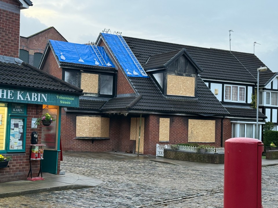 A fire-damaged house with boarded-up windows and a blue tarp on the roof.