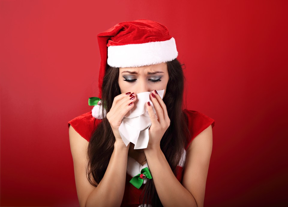 Sad woman in Santa hat blowing her nose.
