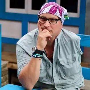 Portrait of a man wearing glasses and a bandana, sitting outdoors.