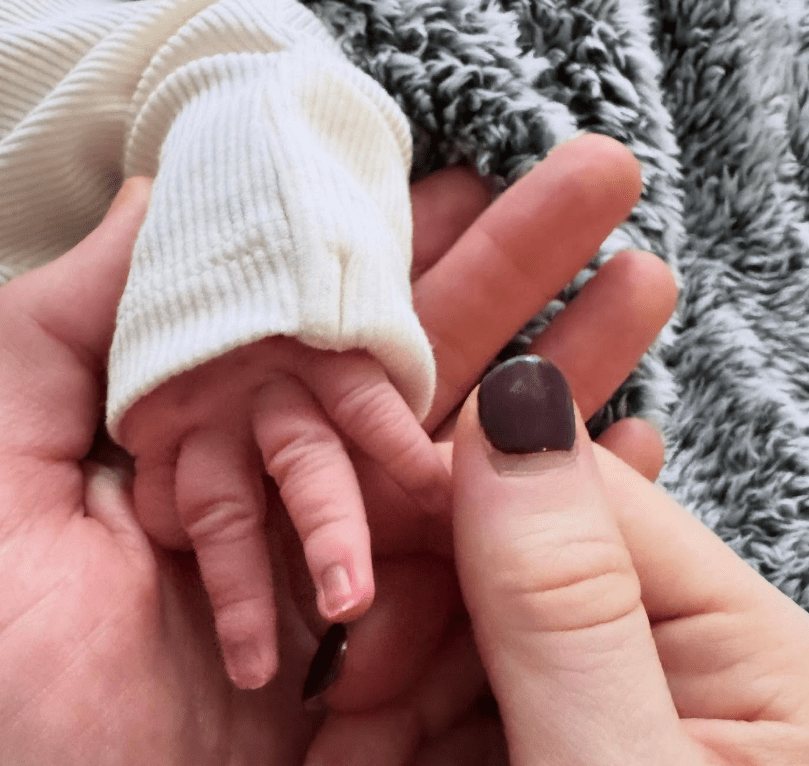 A newborn's hand gently grasping an adult's finger.