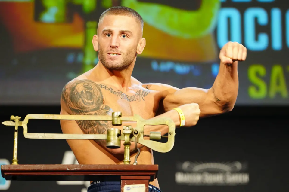 A shirtless man with tattoos weighs in on a vintage scale.