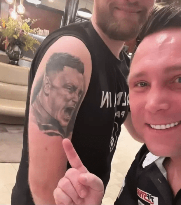 Man showing off a tattoo of a wrestler's portrait on his arm.