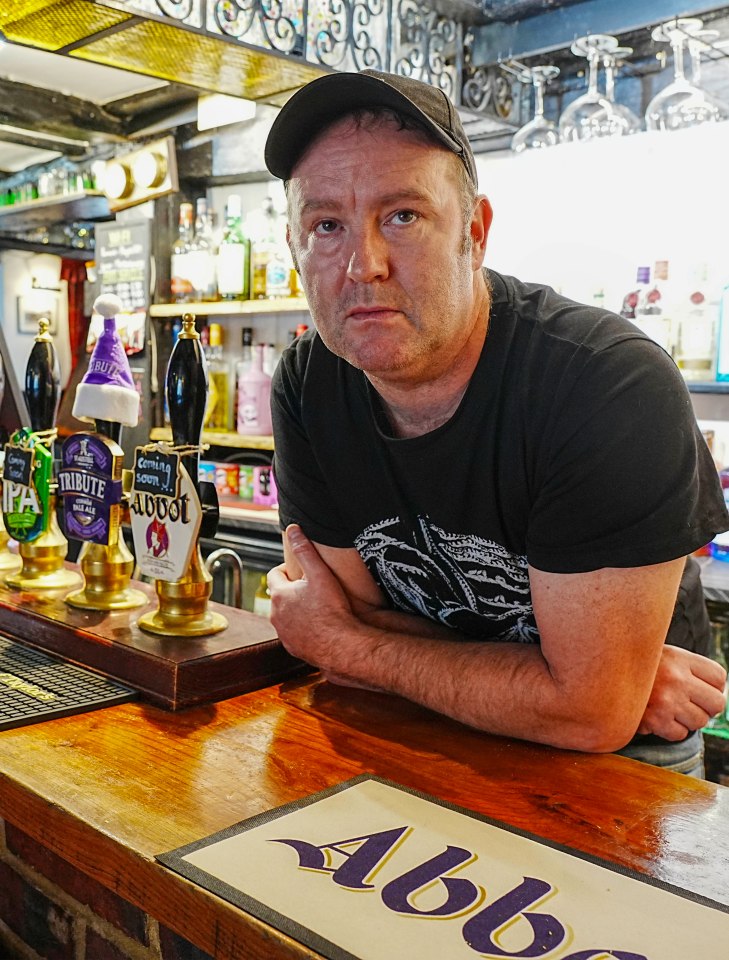 Pub landlord leaning on bar.