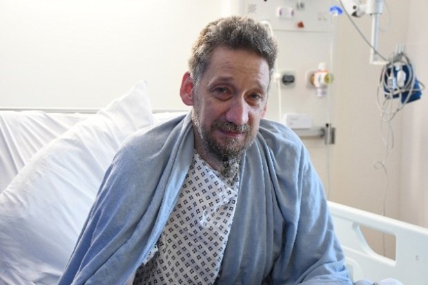 Man in hospital gown sitting in a hospital bed.