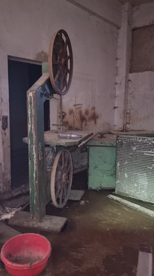 A rusty, old band saw in a dilapidated room.