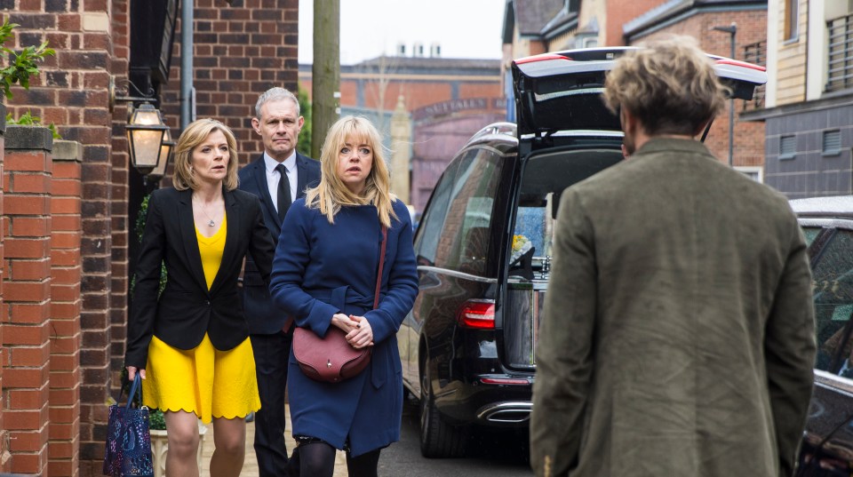 A funeral scene outside an undertaker's; a woman shoves a man and tells him to stay away.