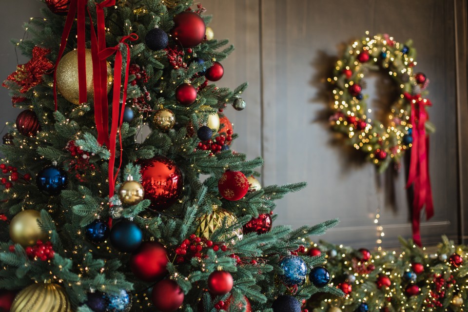 Ornate Christmas tree with red, gold, and blue ornaments and lights, next to a matching wreath.