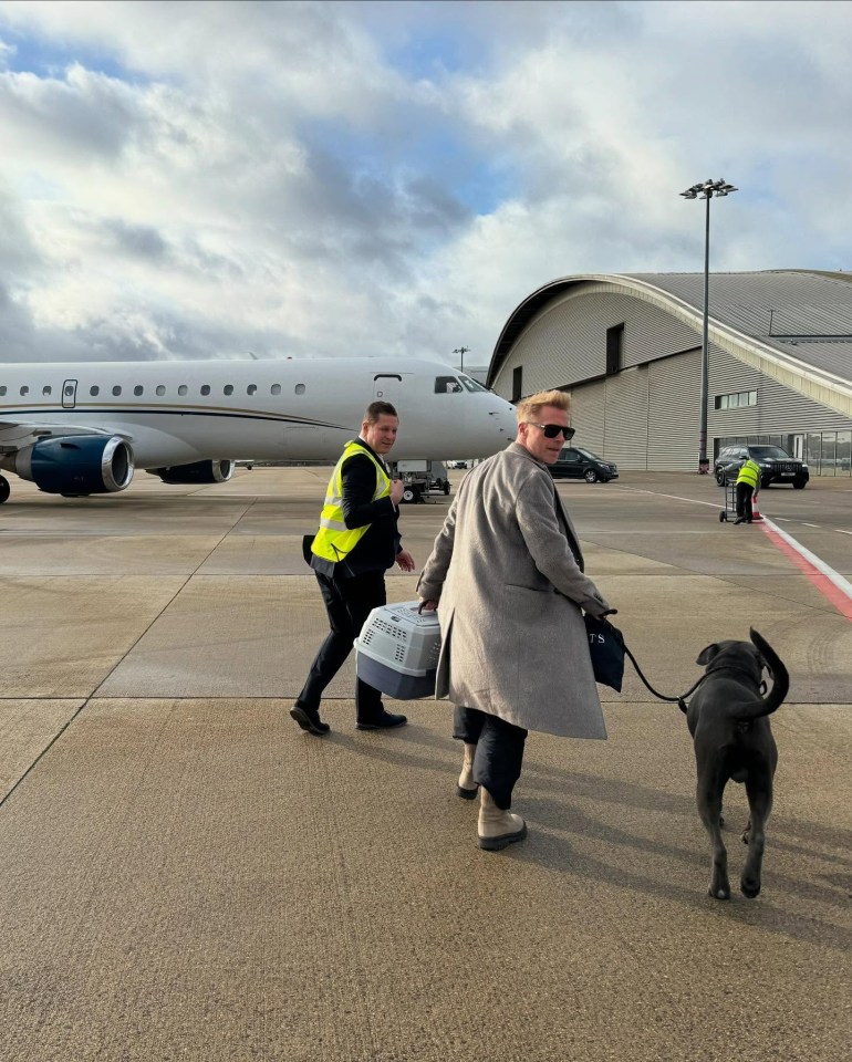Ronan Keating walking a dog and carrying a pet carrier near a private jet.