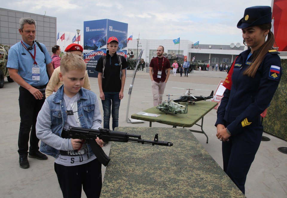 Boy examines AK-74 assault rifle at military exhibition.