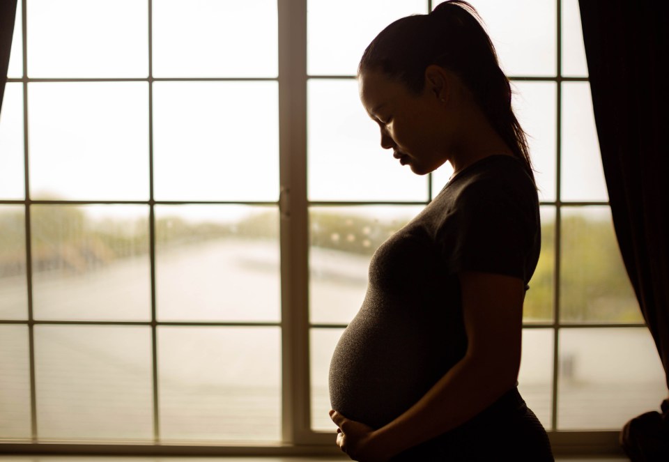 A sad pregnant woman stands by a window.