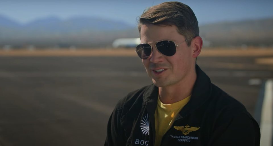 A man in aviator sunglasses speaks on an airfield.
