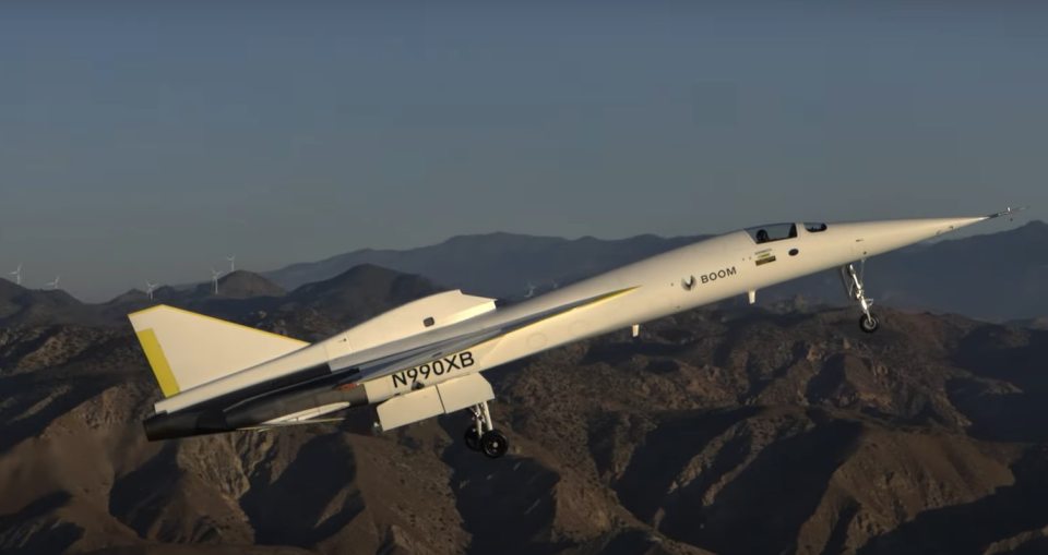 The "Son of Concorde" supersonic jet, N990XB, in flight over a mountainous landscape.
