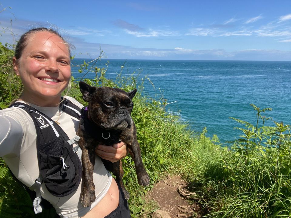 Woman holding a French bulldog near the ocean.