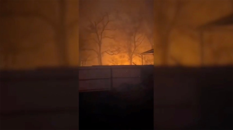 Nighttime fire burning near a fence.