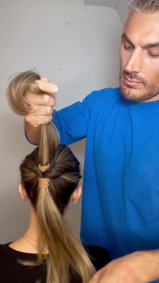 A man styling a woman's hair into a voluminous ponytail.