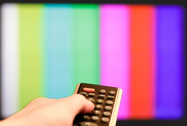 Hand holding TV remote control in front of a television screen displaying a test pattern.