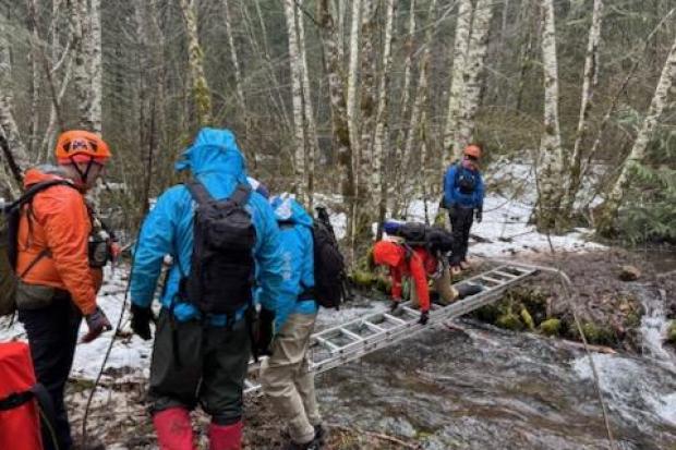 Rescue personnel using a ladder to cross a stream while searching for two missing men.