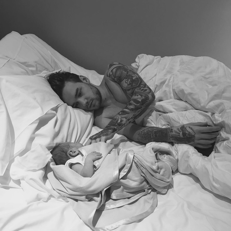 A tattooed man lying in bed with his baby.