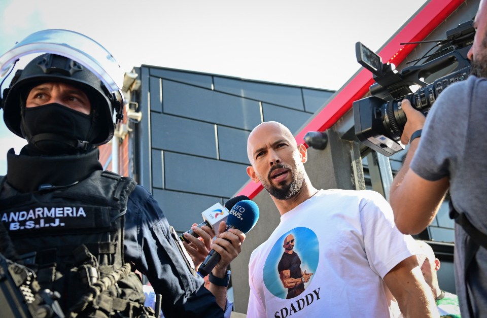 Andrew Tate speaking to journalists outside a building, surrounded by police.